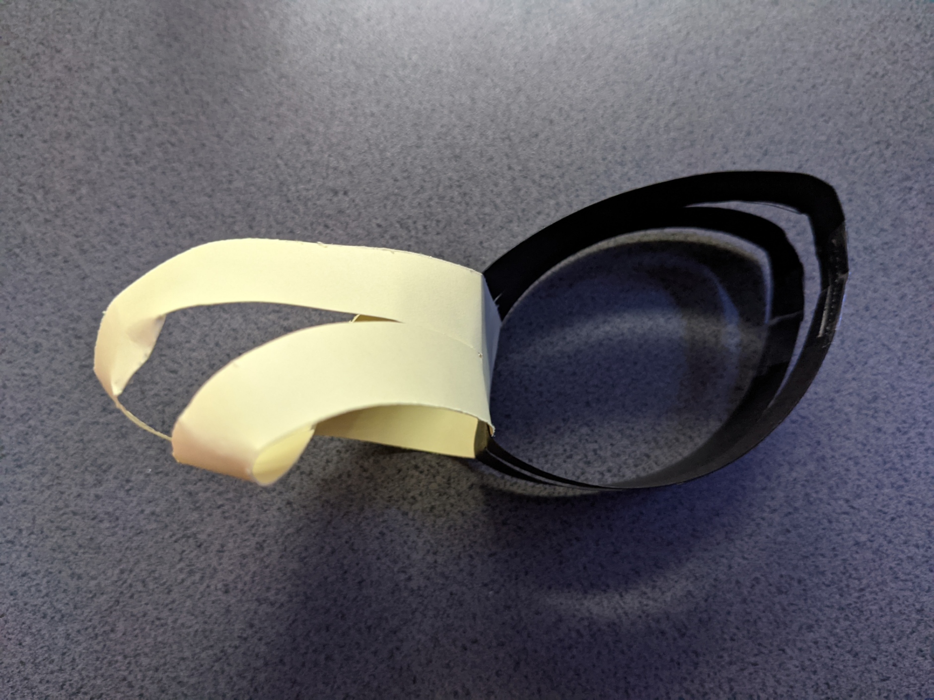 A simple loop of black card attached at right-angles to a Möbius Strip. Both have been cut along the strips' centre lines round from and to where they are joined.